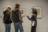 Zwei Männer und eine Frau stehen vor Bildern im Ausstellungsraum und unterhalten sich.
