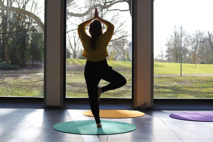 Frau in Yoga-Position steht im dem Gartensaal des Clemens Sels Museum Neuss und blickt in den Park