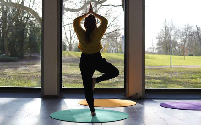 Frau in Yoga-Position steht im dem Gartensaal des Clemens Sels Museum Neuss und blickt in den Park
